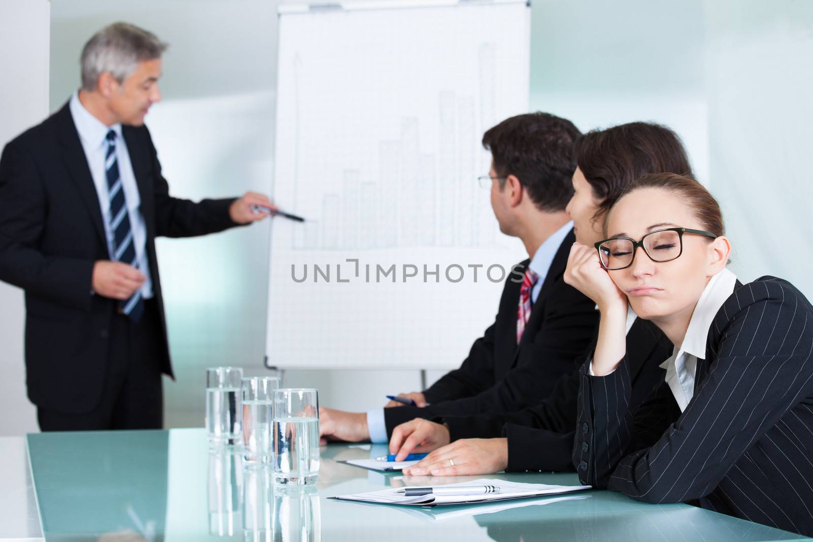 Bored businesswoman sleeping in a meeting as her colleague who is giving the presentation talks in the background