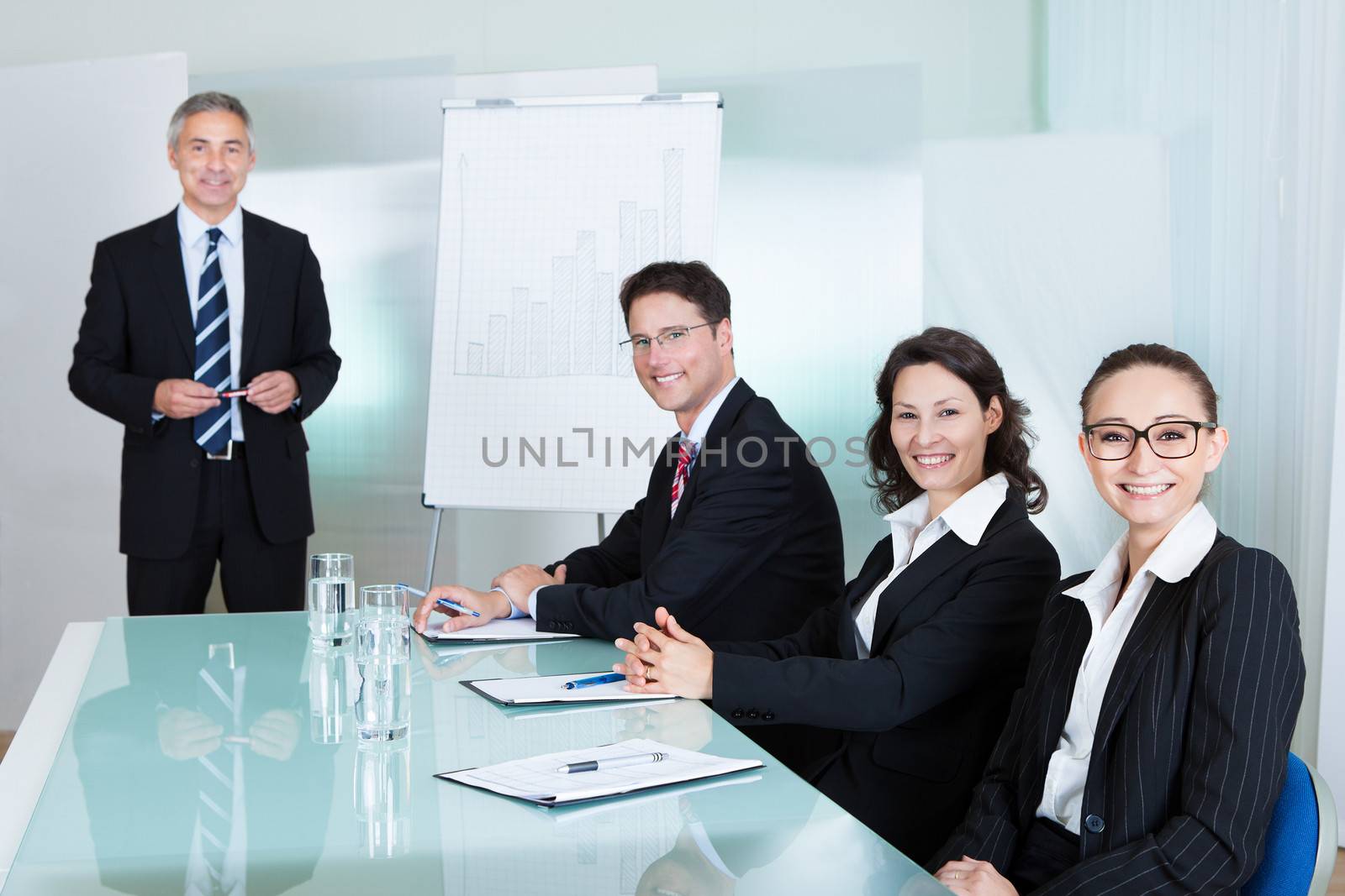 Smiling successful business team holding a meeting sitting around a white glass topped table with one executive