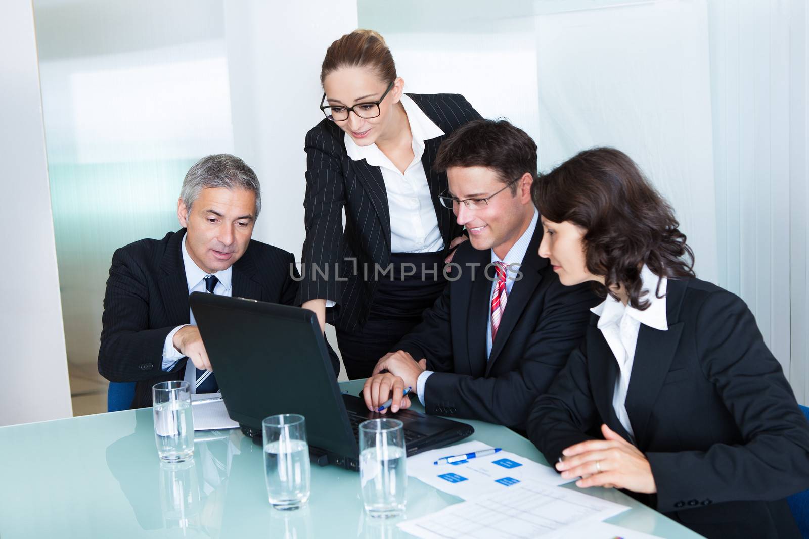 Business team of professional men and women have a meeting gathered around a laptop computer surrounded by literature