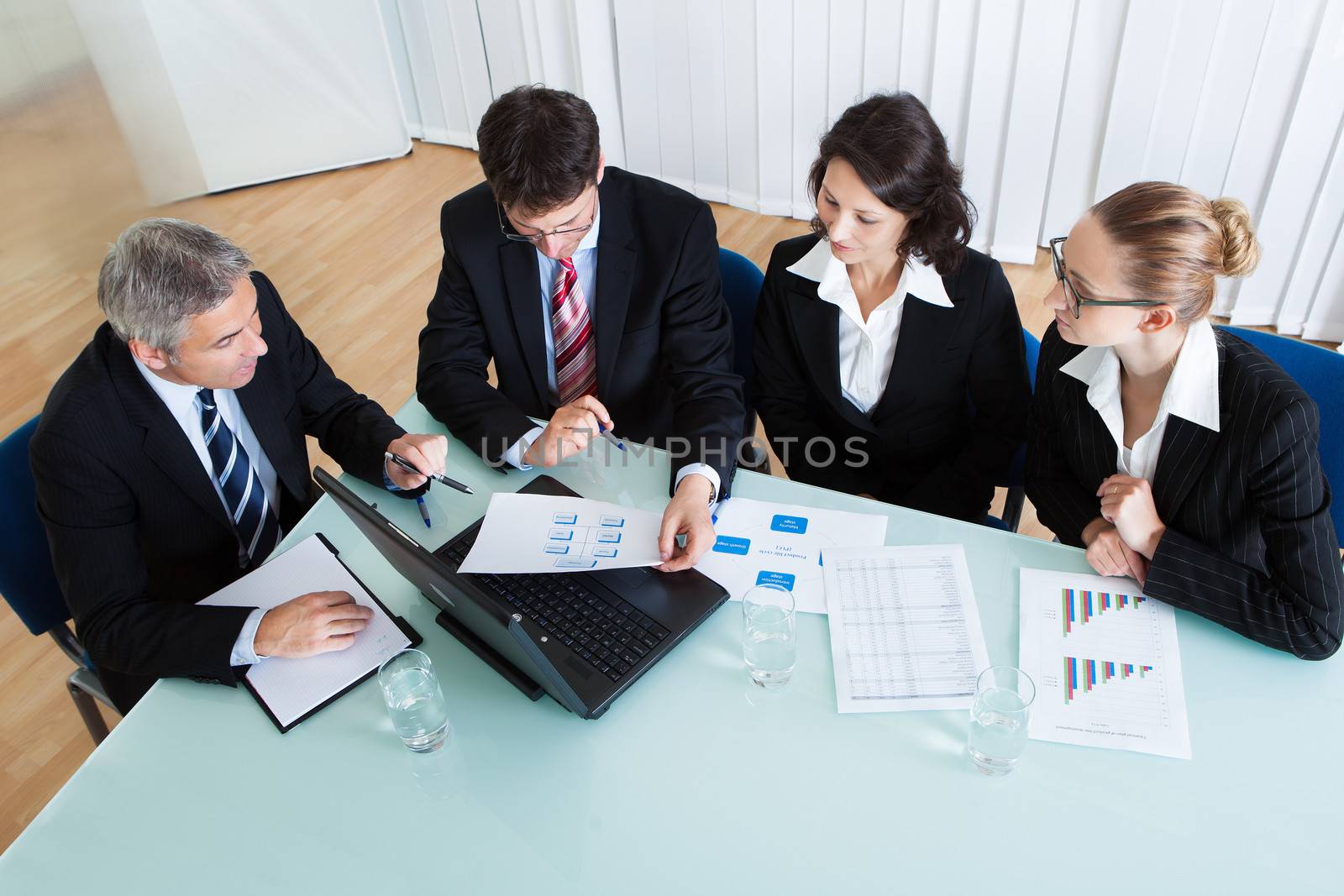 Overhead view of a group of diverse business executives holding a meeting around a table discussing graphs showing statistical analysis