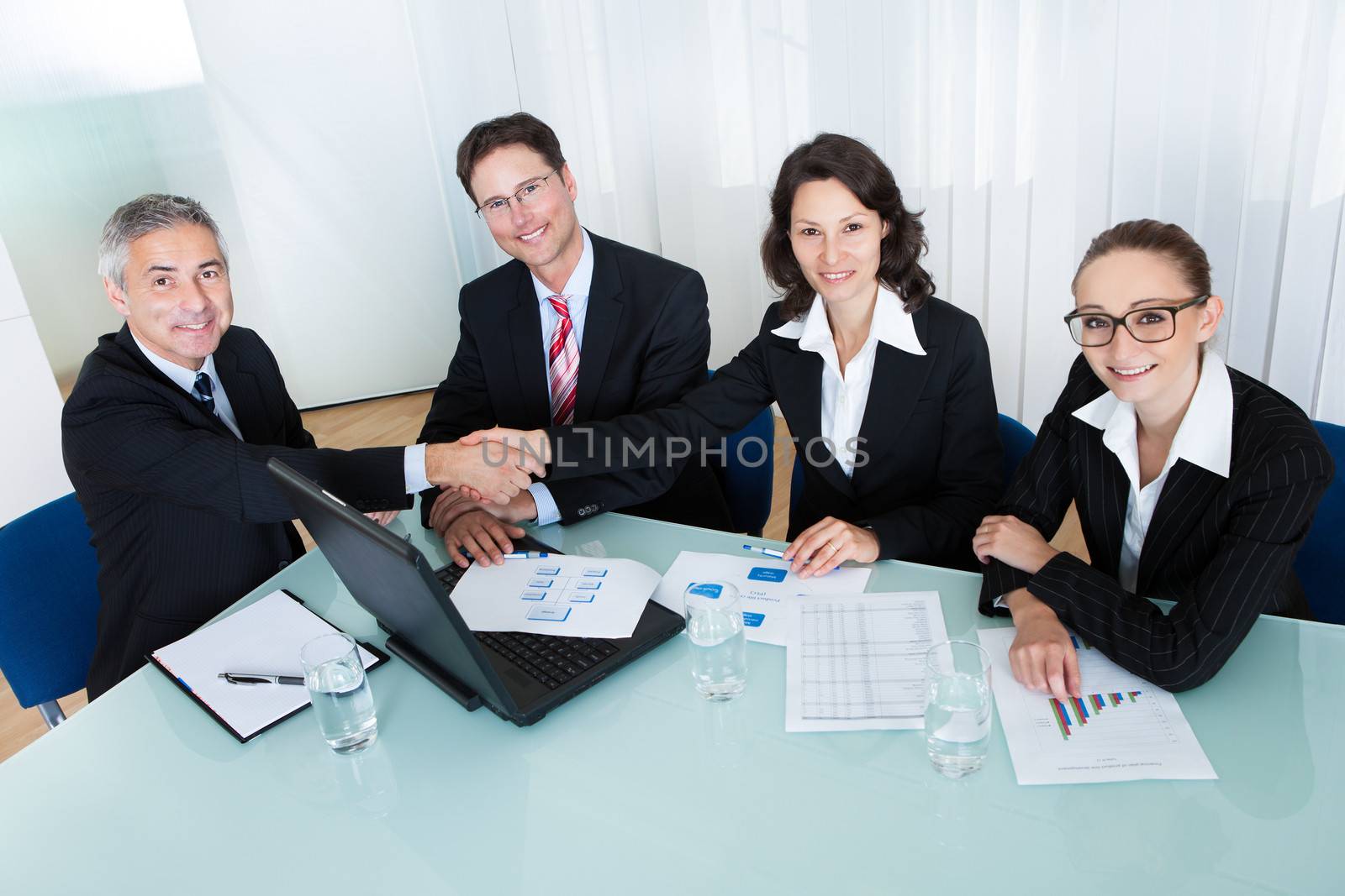 Business colleagues seated around a table in a meeting congratulating one another by shaking hands
