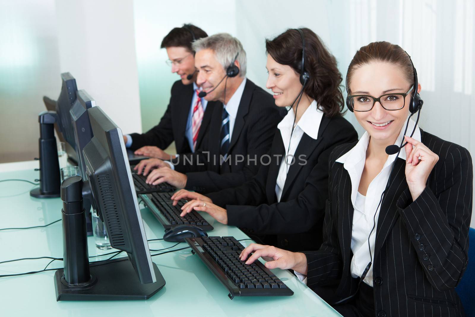 Line of professional stylish call centre operators wearing headsets seated behind their computers giving assistance