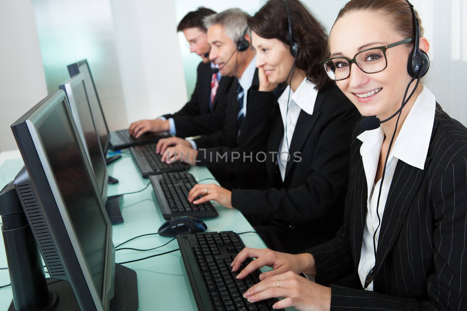 Line of professional stylish call centre operators wearing headsets seated behind their computers giving assistance