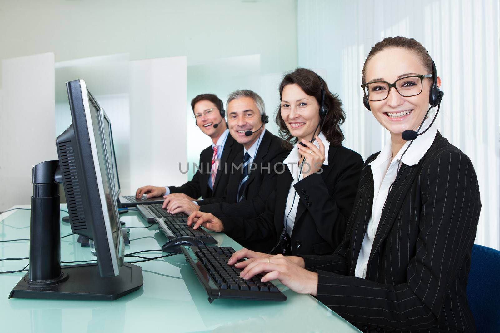 Line of professional stylish call centre operators wearing headsets seated behind their computers giving assistance