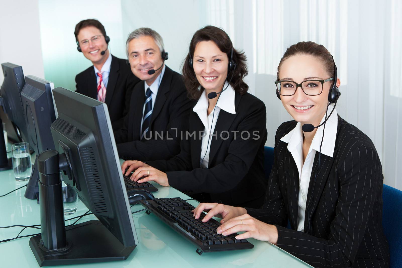 Line of professional stylish call centre operators wearing headsets seated behind their computers giving assistance