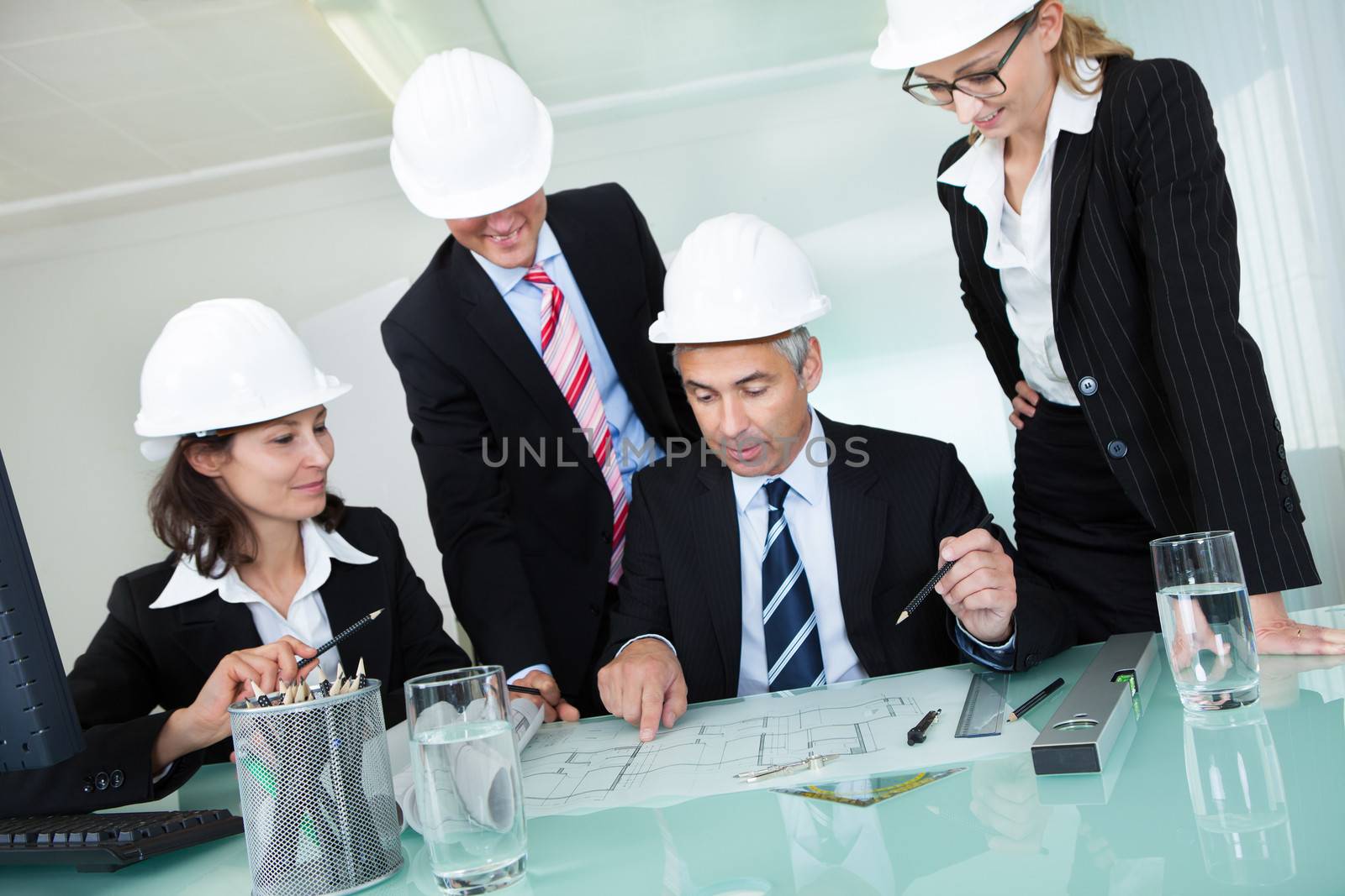 Meeting of four diverse architects or structural engineers in hardhats and suits seated in an office