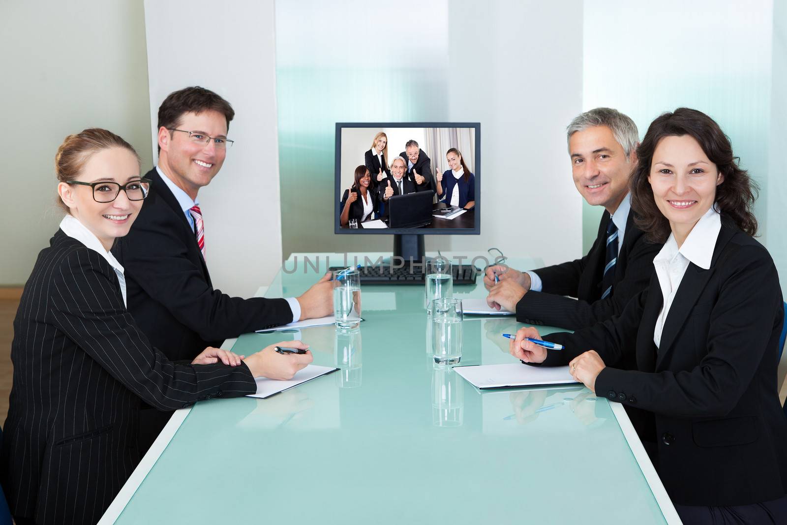 Group of male and female businesspeople seated at a table watching an online presentation on a computer screen