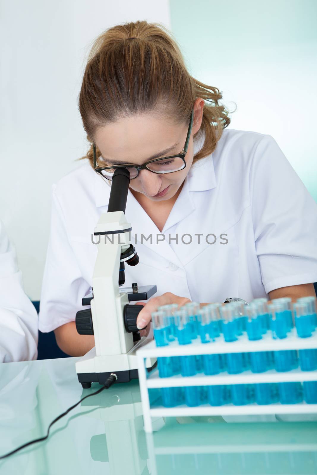Female laboratory technician using a monocular microscope to read test results which she is recording on paper
