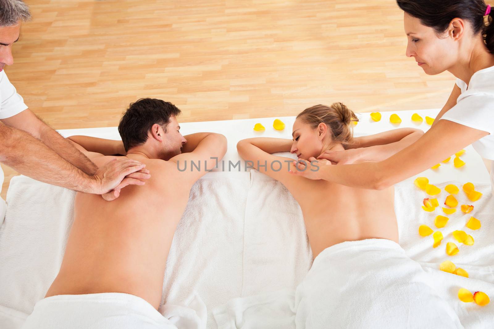 Young couple relaxing and enjoying a joint back massage at a spa and the woman is surrounded by yellow flower petals