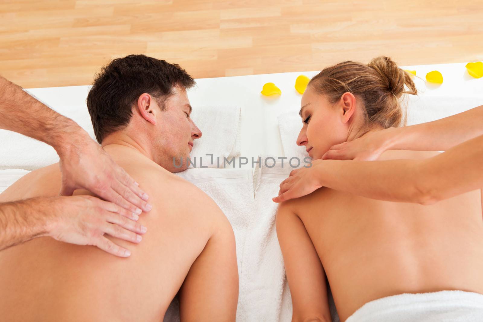 Young couple relaxing and enjoying a joint back massage at a spa and the woman is surrounded by yellow flower petals