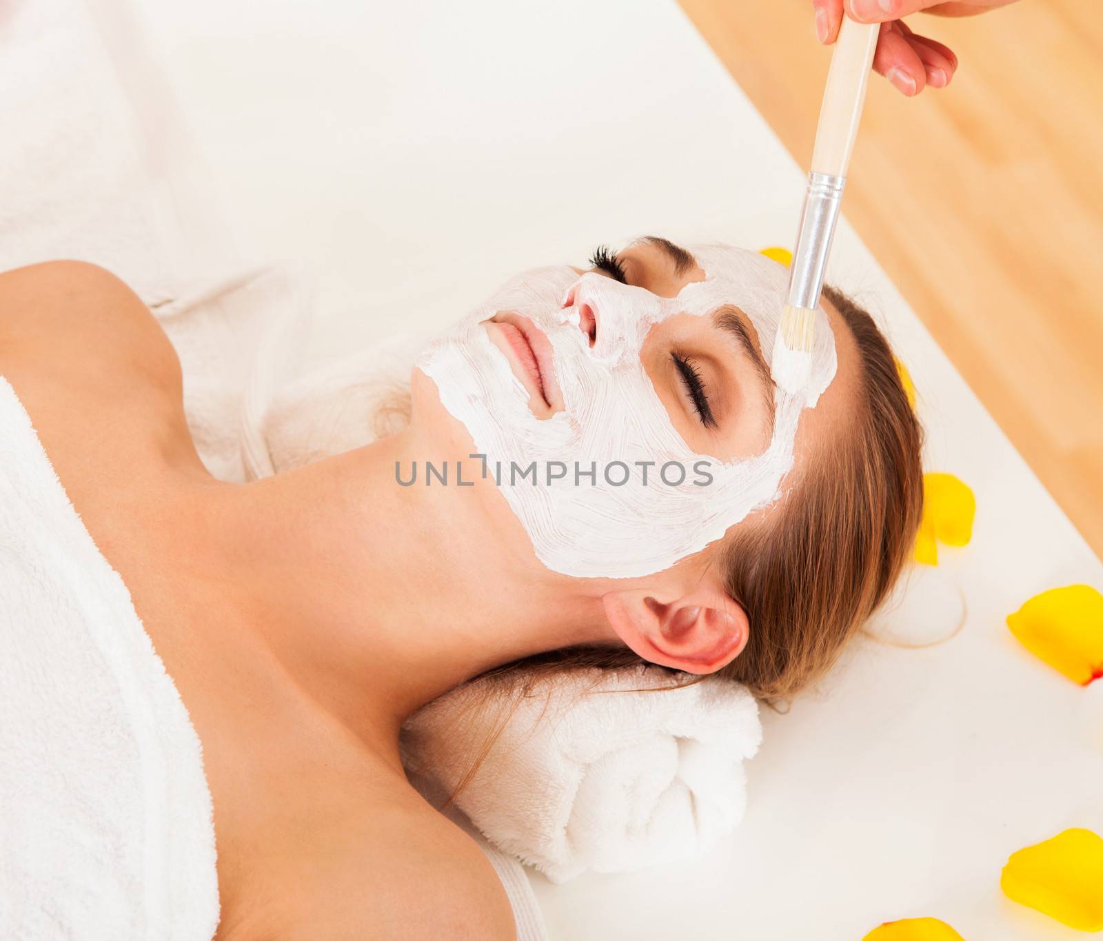 Therapist applying a face mask to the face of a beautiful young blonde woman using a cosmetic brush