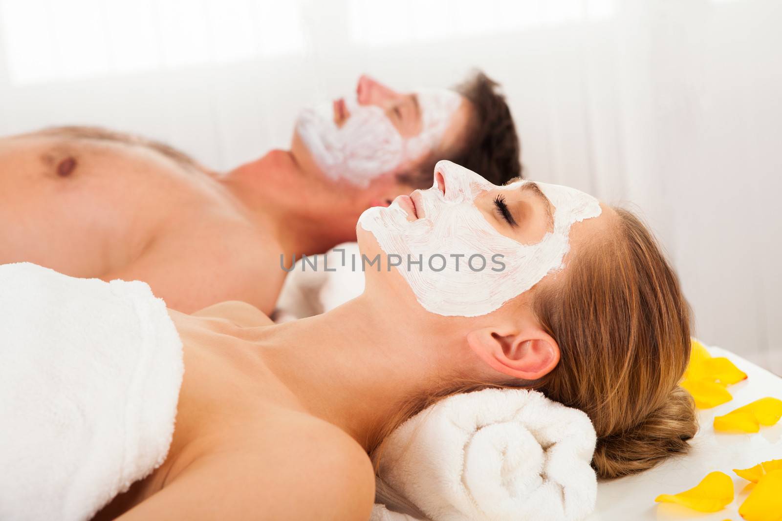 Man and woman in face masks lying back on clean white towels in a spa relaxing