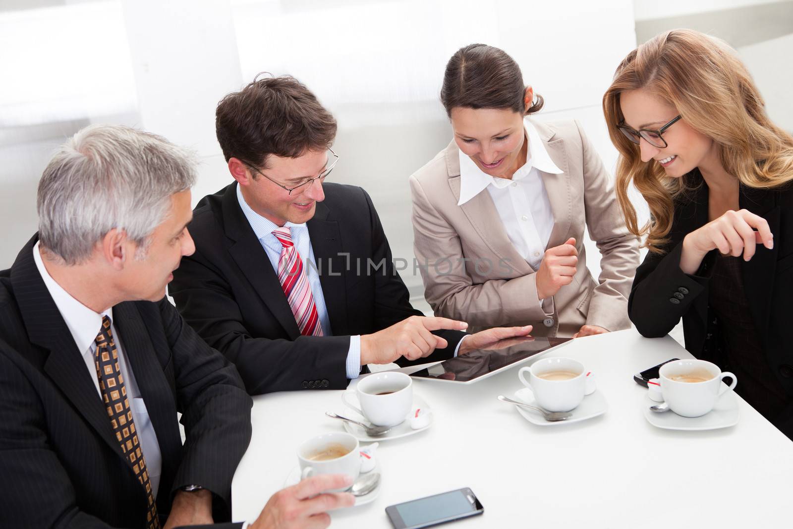 Business colleagues enjoying a coffee break smiling at something on the screen of a tablet held by one of the men