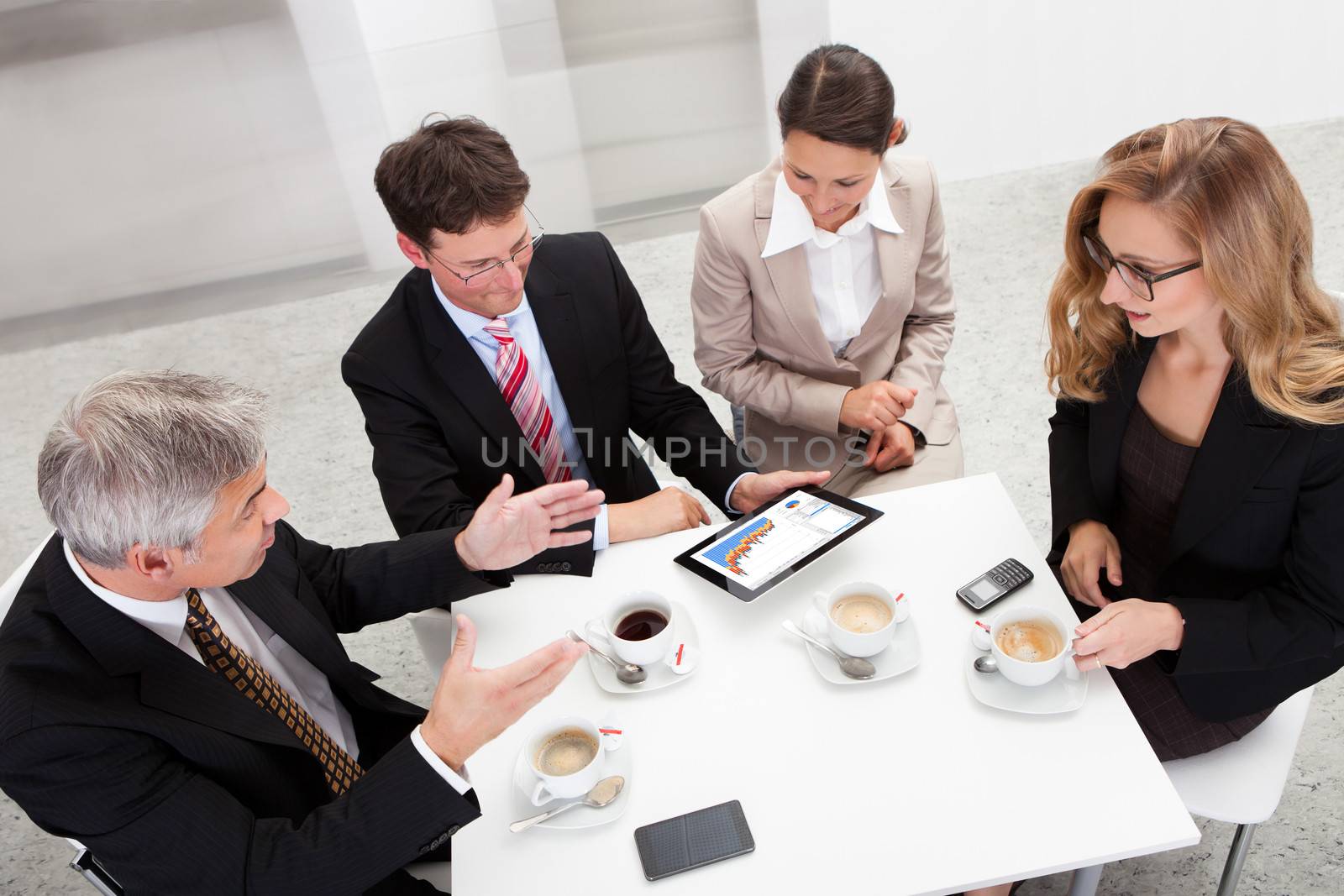Business colleagues enjoying a coffee break smiling at something on the screen of a tablet held by one of the men