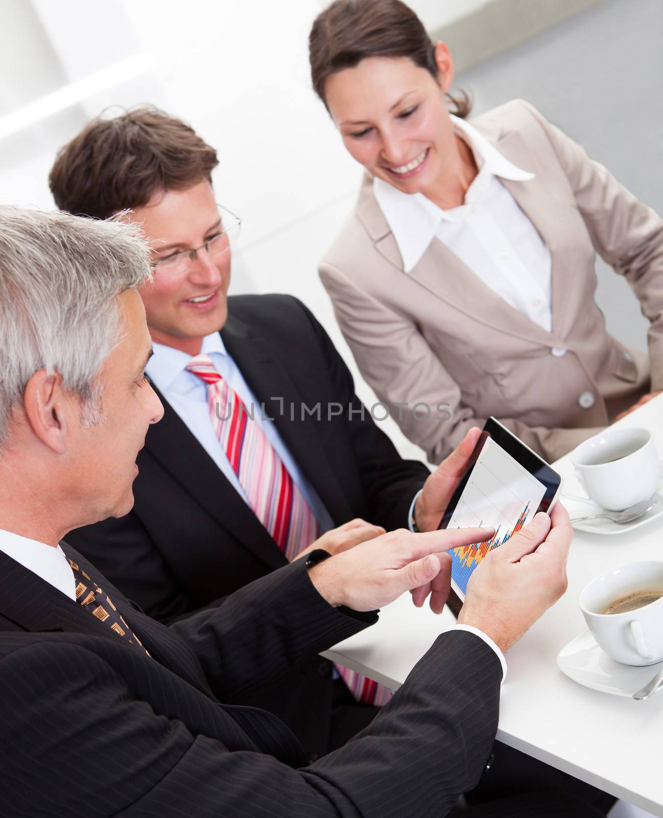 Business colleagues enjoying a coffee break smiling at something on the screen of a tablet held by one of the men