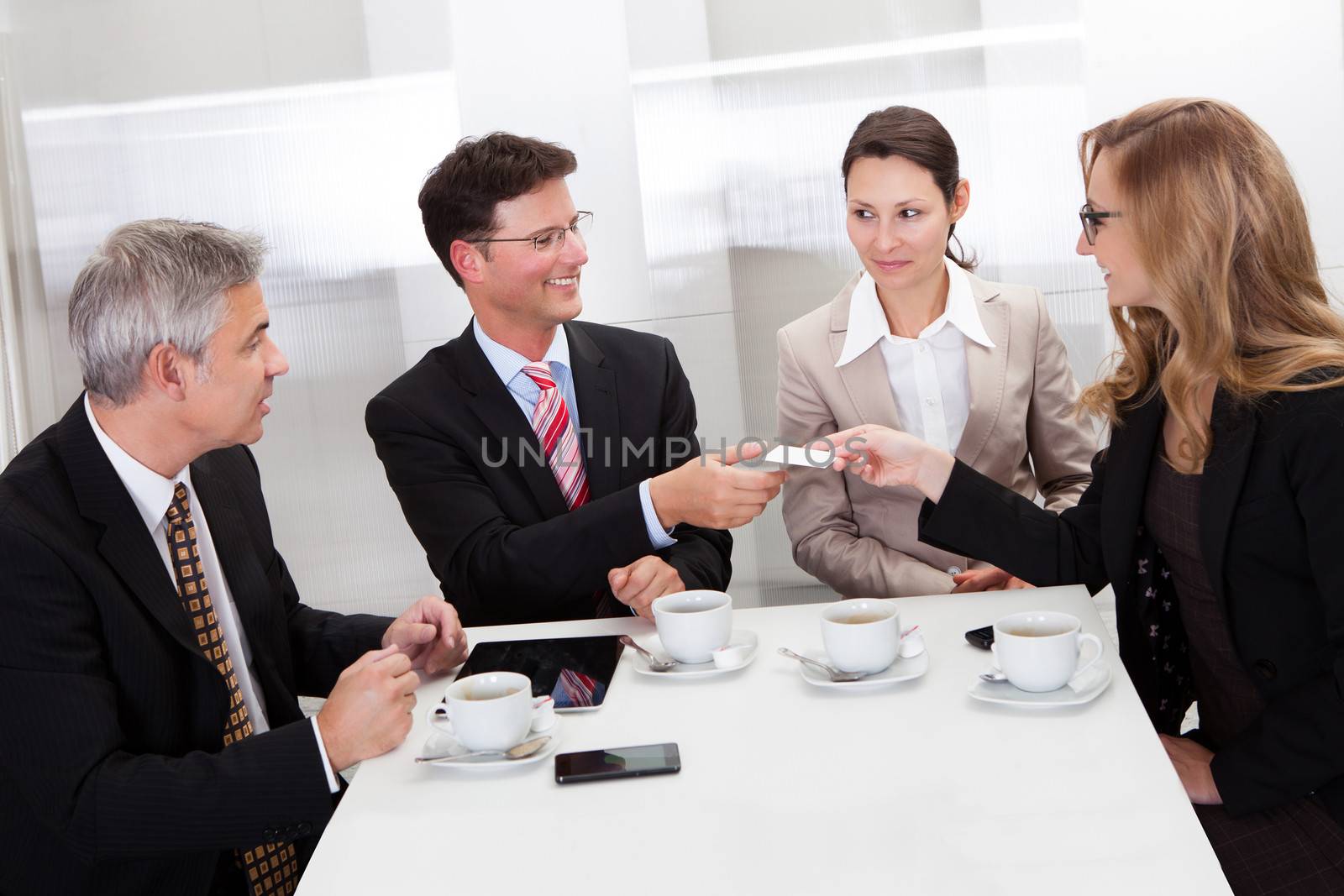 Businesspeople exchanging cards over coffee while having an informal meeting in a cafe