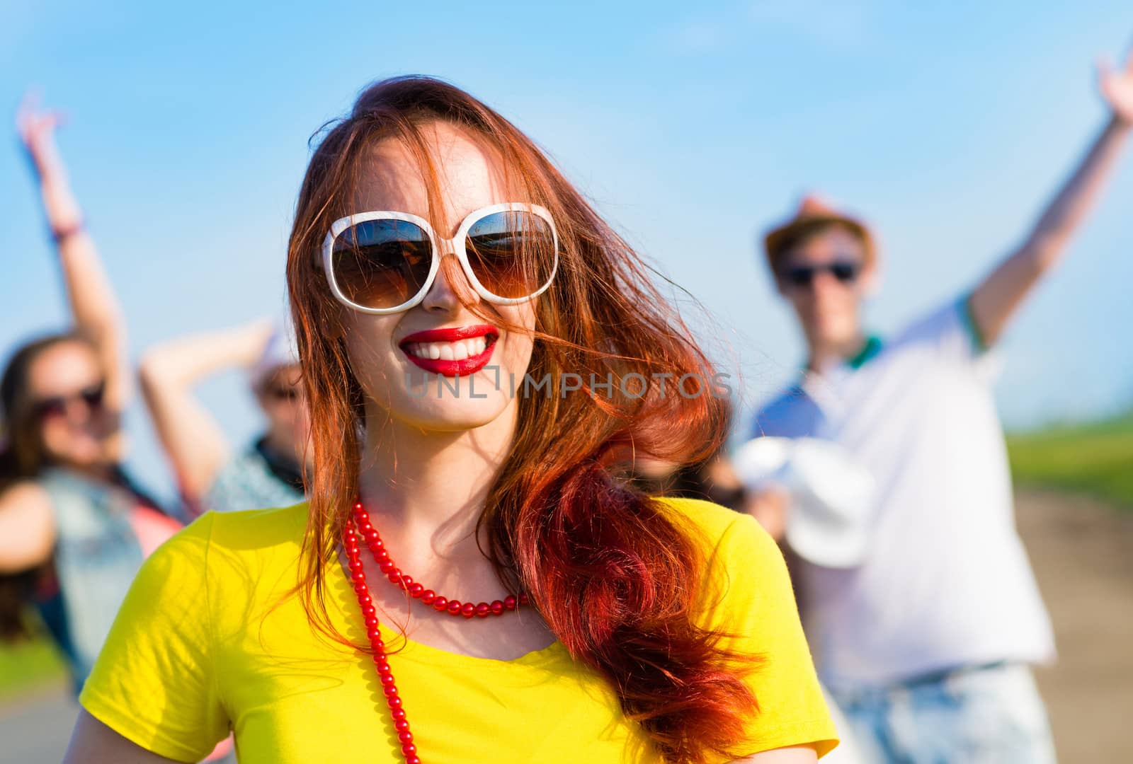 stylish young woman in sunglasses on the background of blue sky and friends