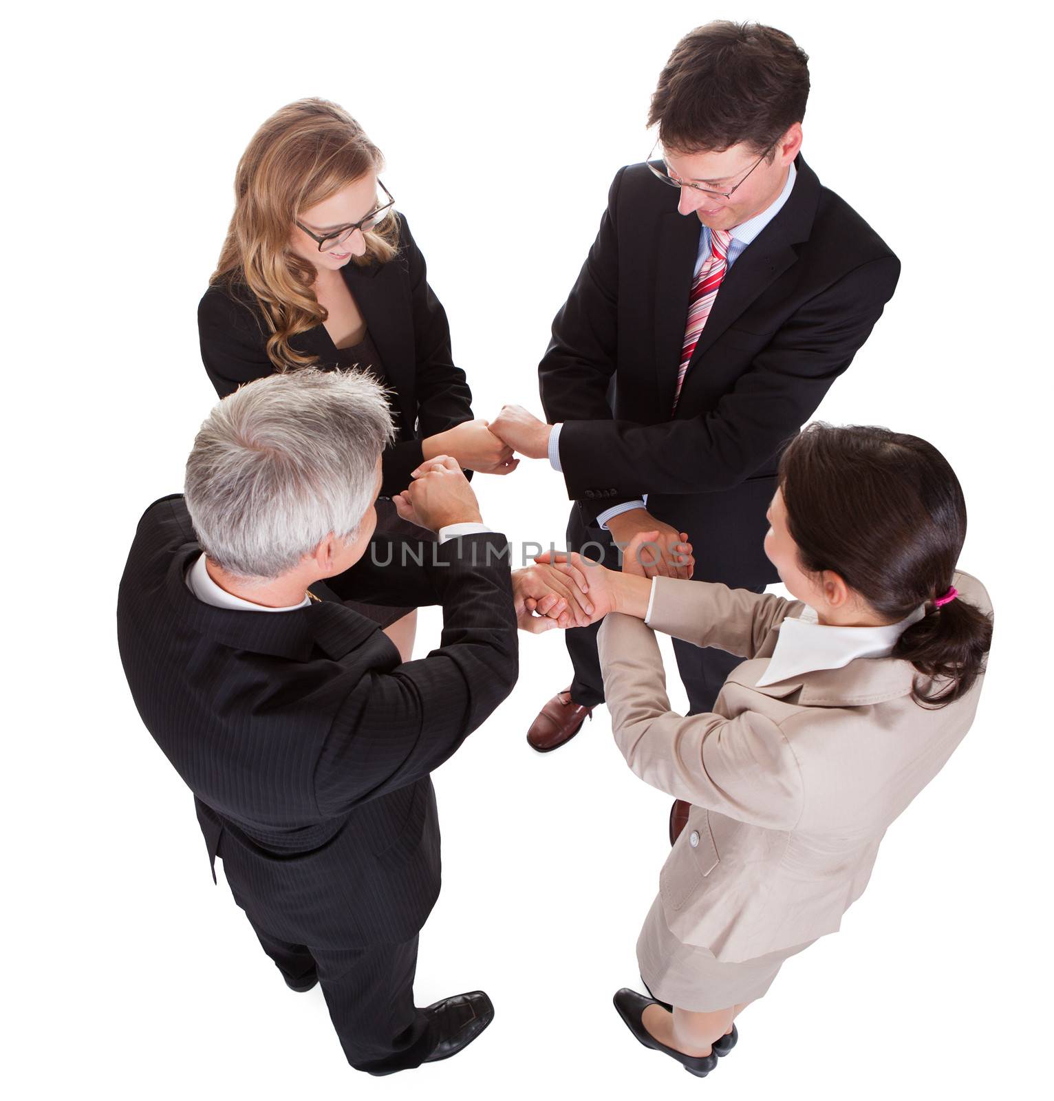 Group of four diverse businesspeople standing in a circle facing each other holding hands in a team