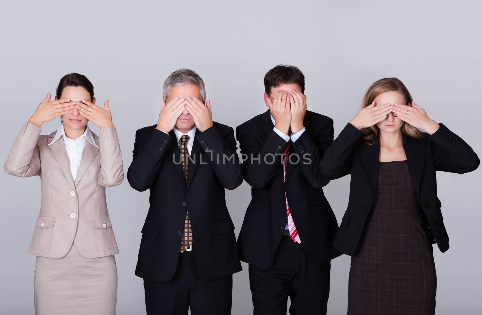 Four diverse businesspeople standing in a row holding their eyes shut in a conceptual representation of the saying - See no evil