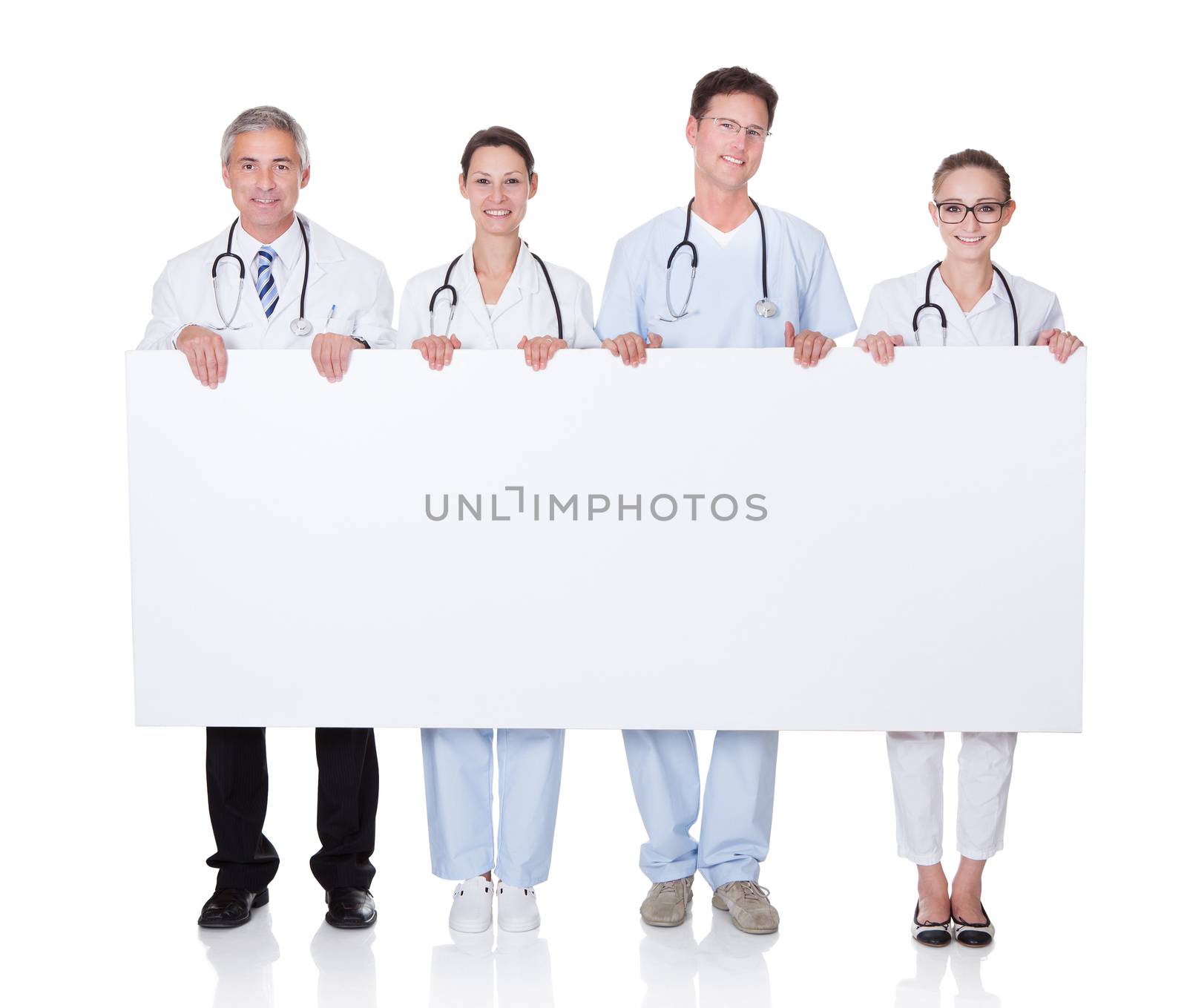 Four attractive professional diverse medical staff holding up a long horizontal blank white banner for your text or advertisement