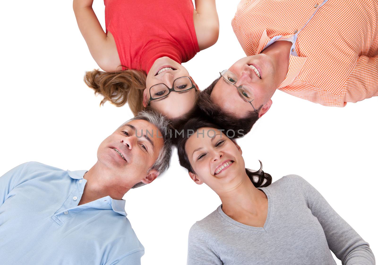 Conceptual image of four smiling middle-aged friends facing inwards with their heads together looking down at the camera isolated on white