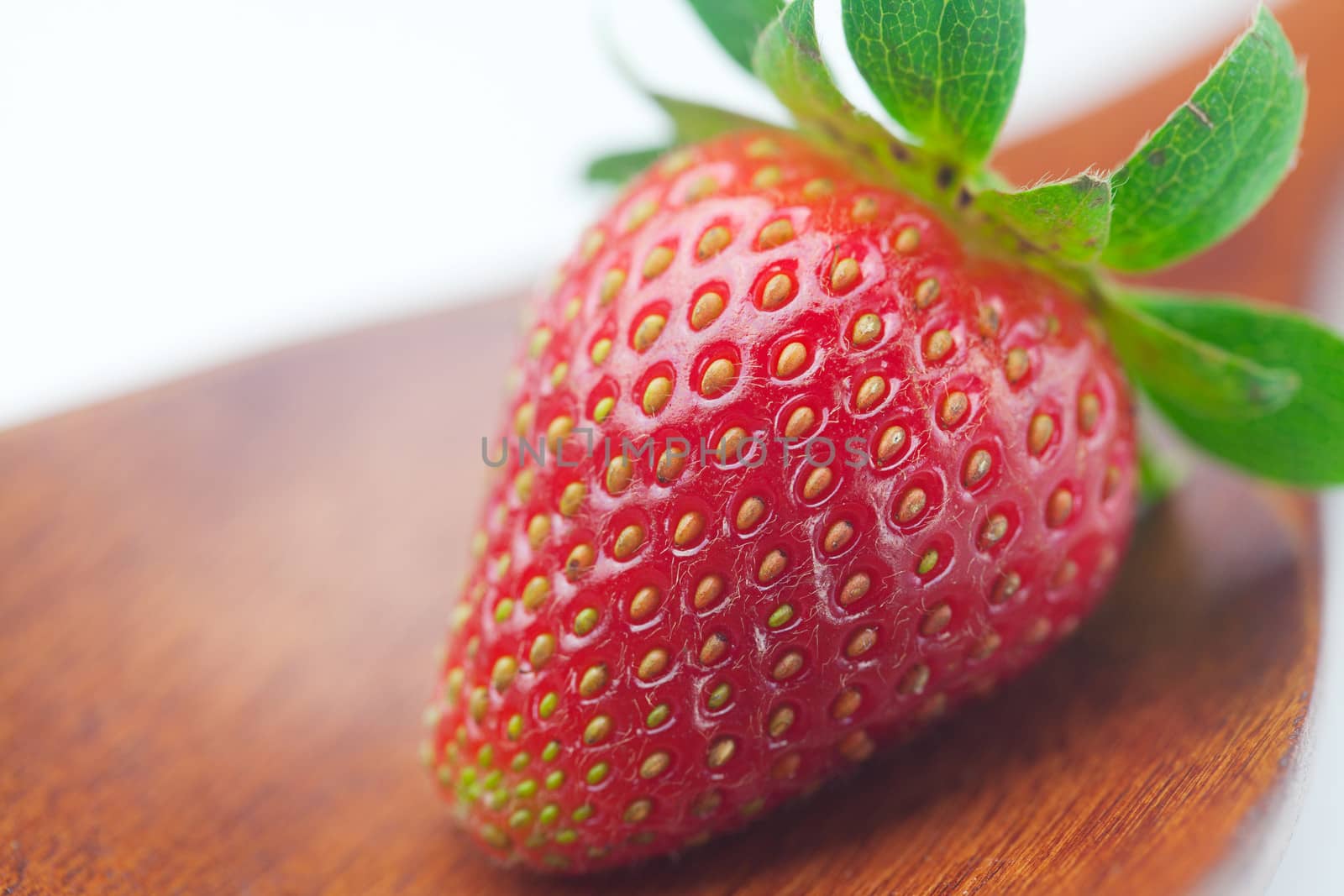 Beautiful ripe strawberry on a wooden spoon isolated on white by jannyjus