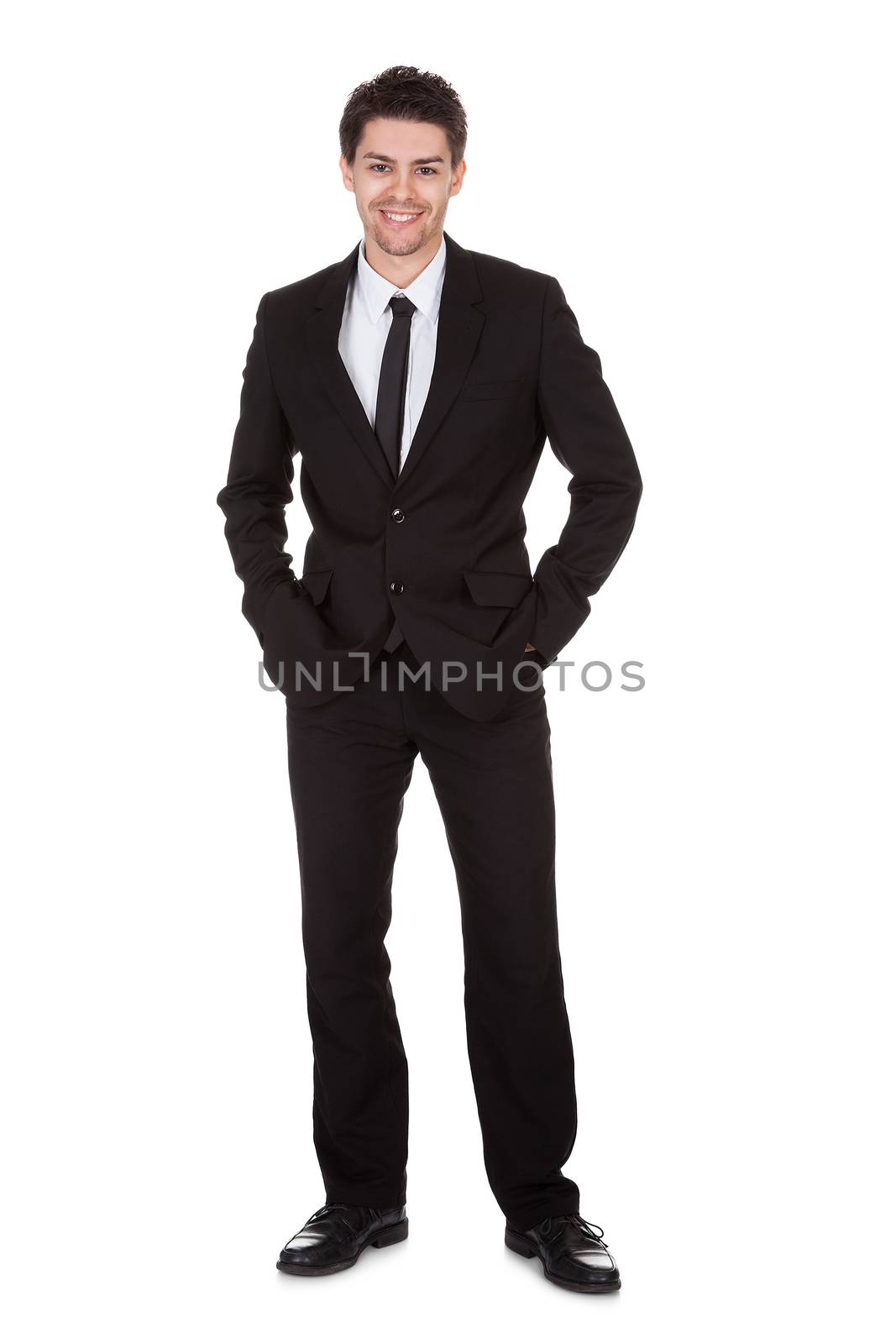 Full length studio portrait on white of a smiling confident young businessman standing with folded arms