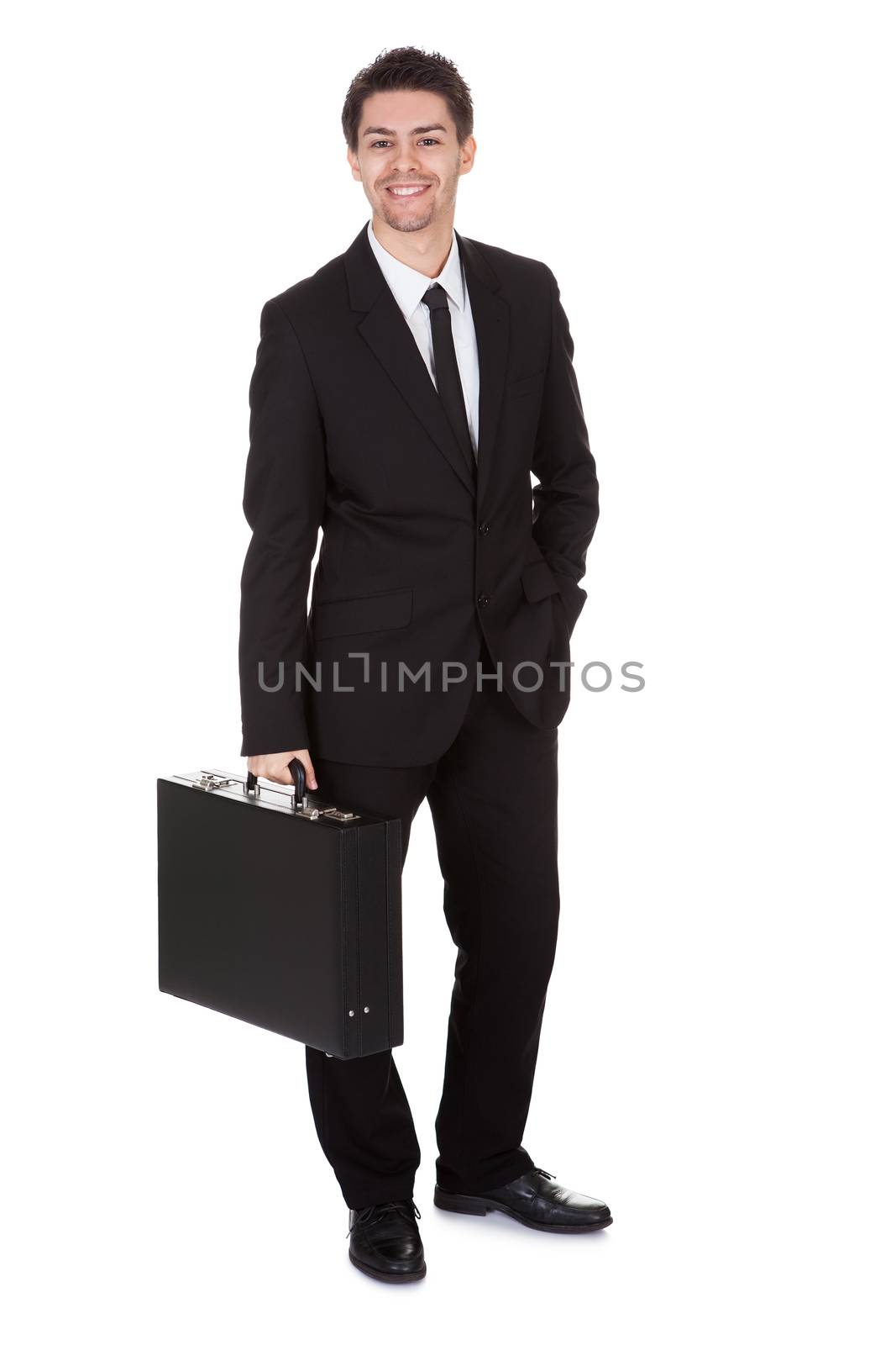 Full length studio portrait on white of a smiling confident young businessman standing with suitcase