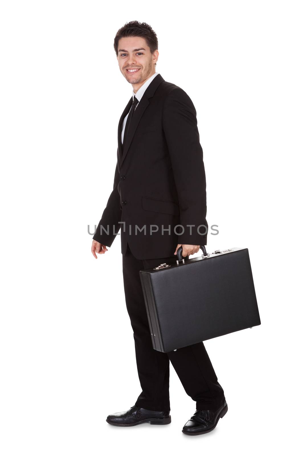 Full length studio portrait on white of a smiling confident young businessman standing with suitcase