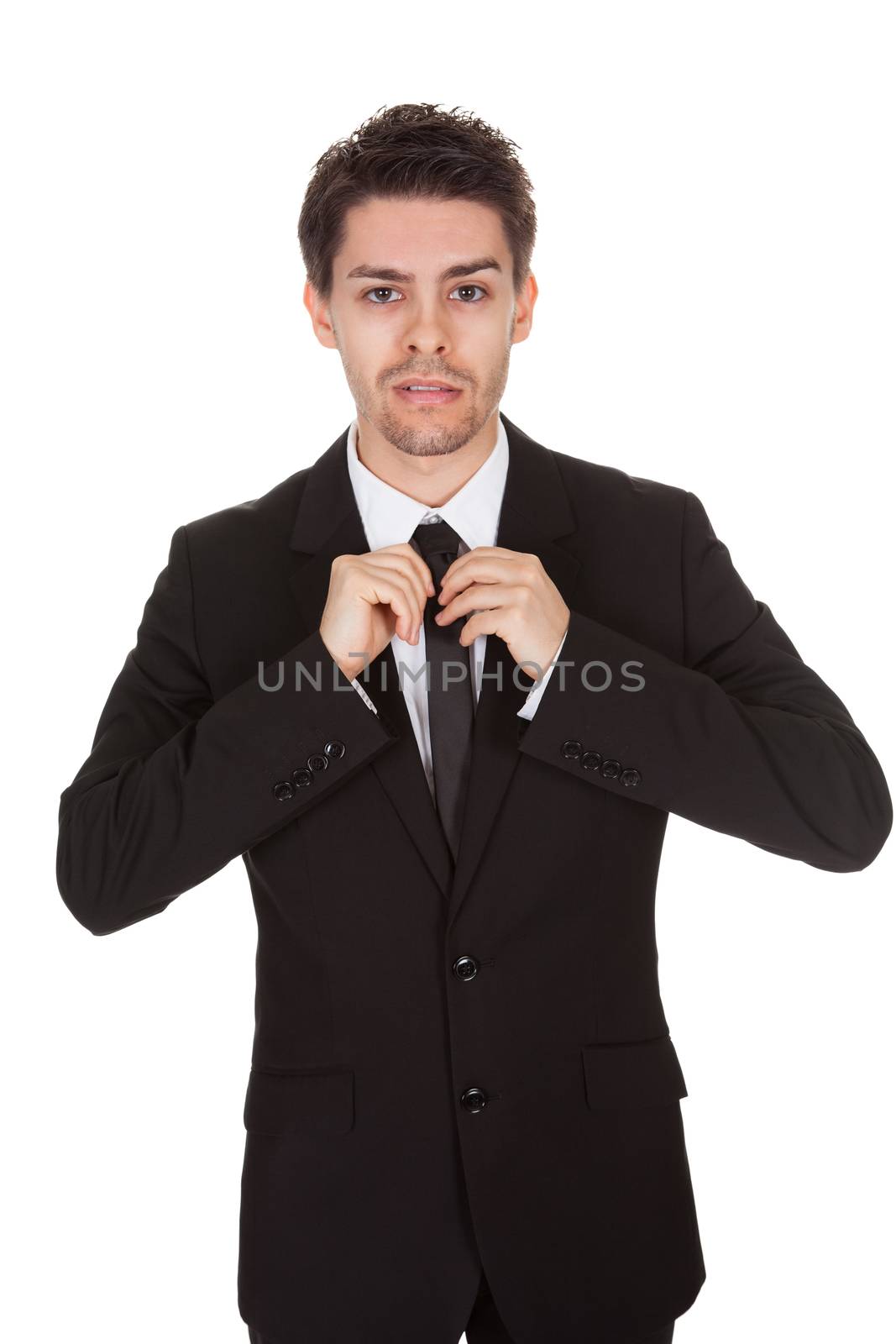 Half body portrait of a handsome young businessman standing straightening his tie isolated on white