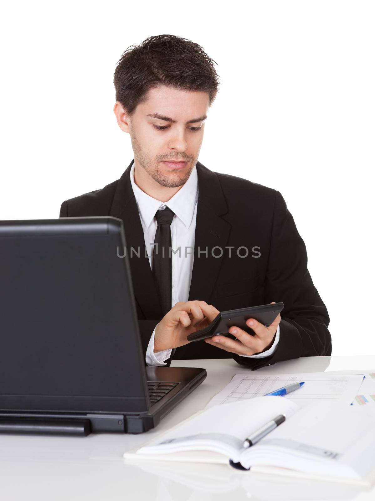 Smiling good looking young accountant sitting at his desk making calculations on a handheld calculator