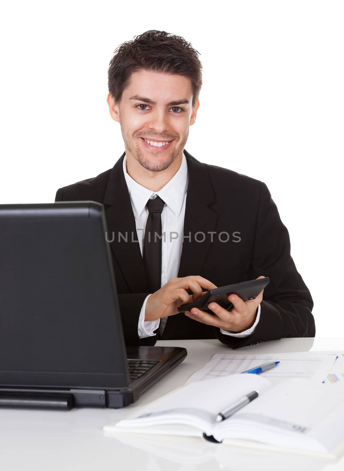 Smiling good looking young accountant sitting at his desk making calculations on a handheld calculator