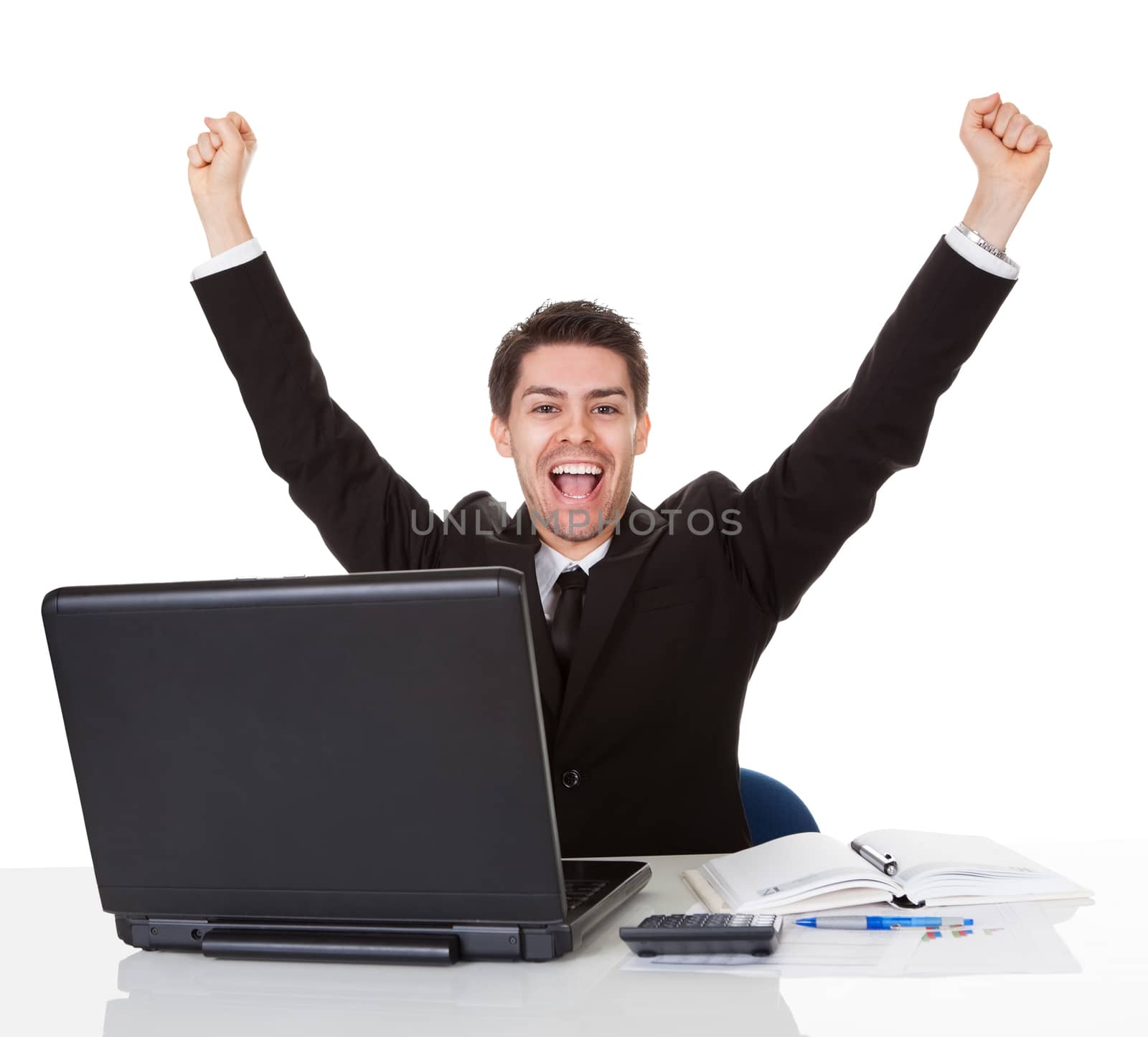 Businessman sitting at his desk rejoicing throwing his arms up in the air and shouting with glee at his success