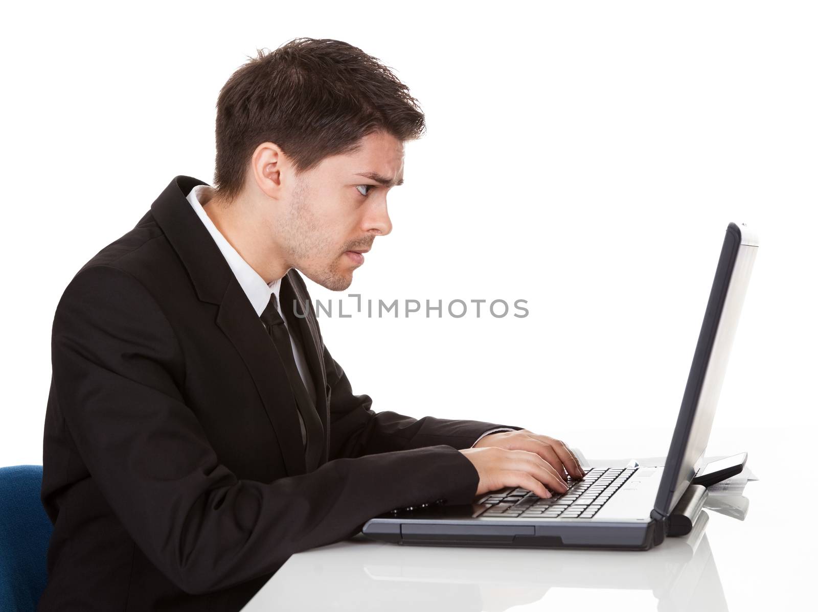 Young handsome young businessman seated at his desk behind his laptop computer looking at the camera