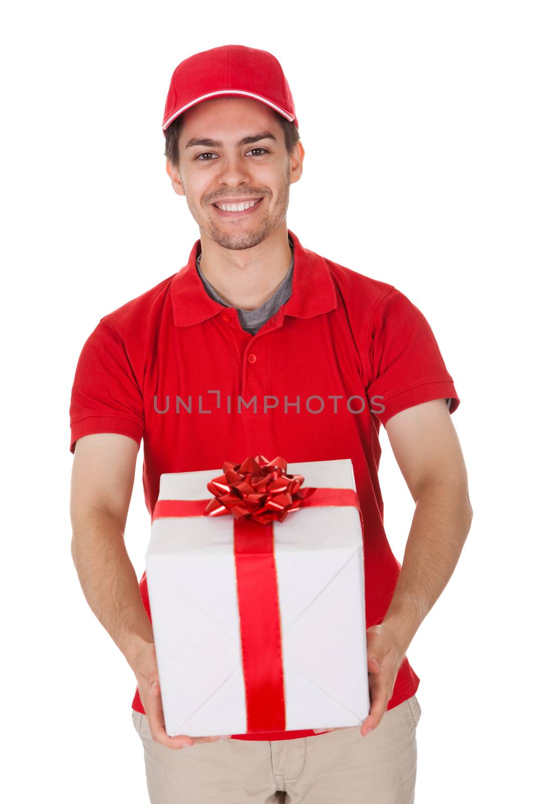 Cheerful smiling young male messenger delivering a decorative gift isolated on white