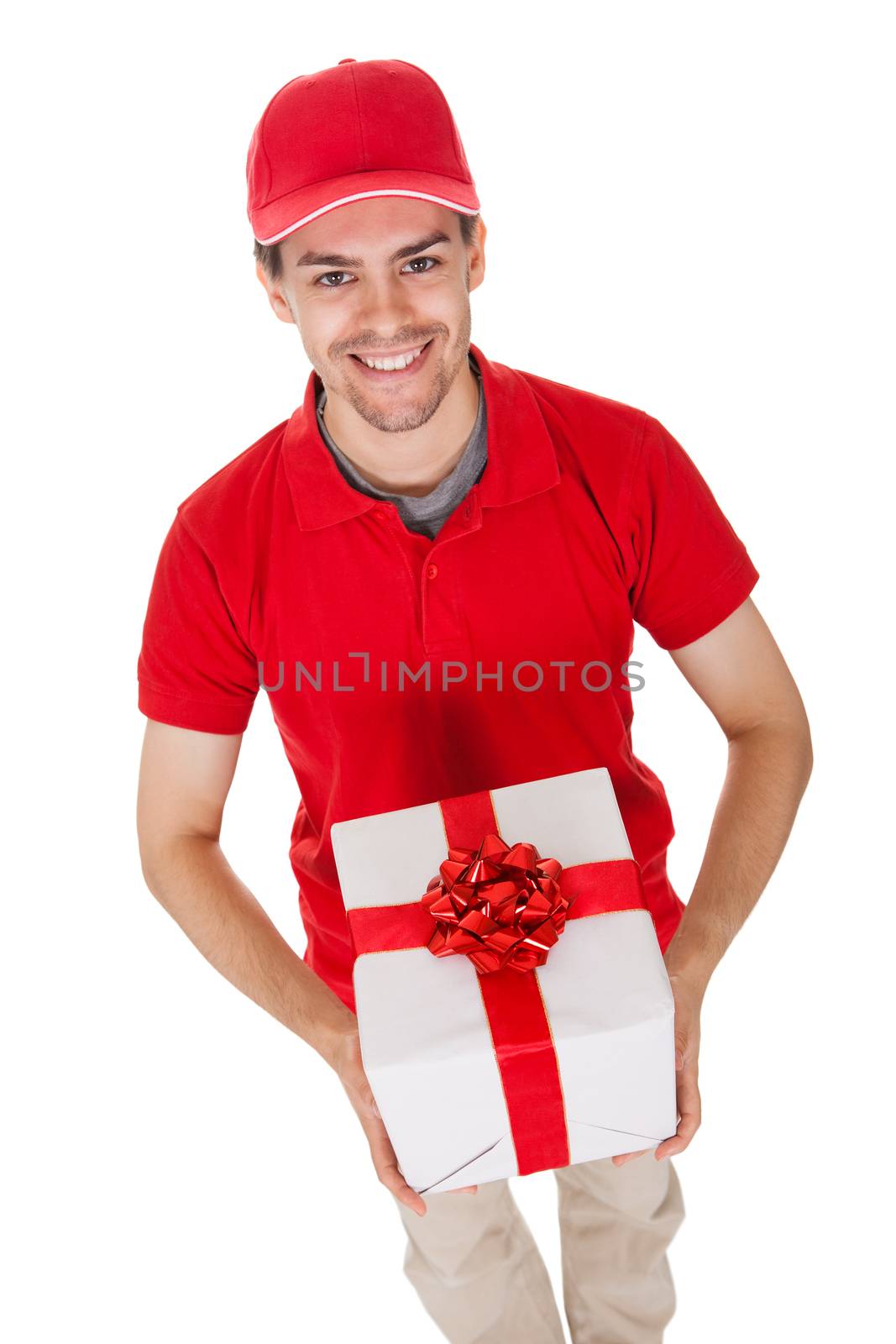 Cheerful smiling young male messenger delivering a decorative gift isolated on white