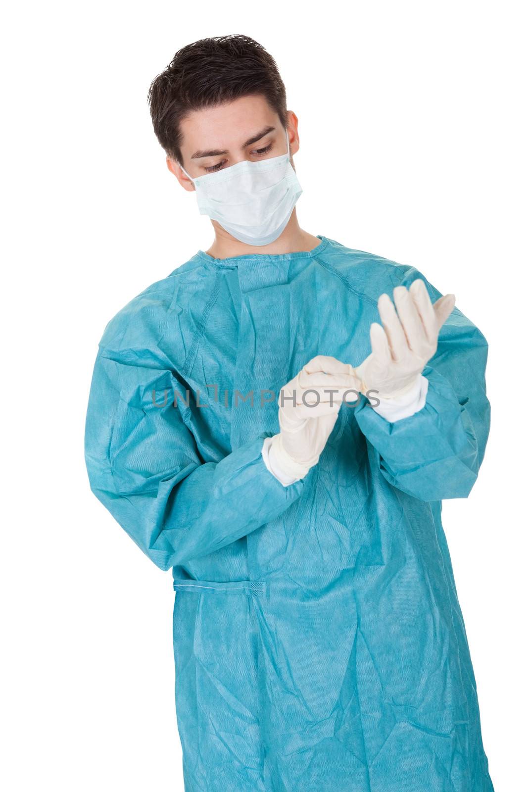 Young male surgeon in a mask and gown putting on disposable surgical gloves before going in to theatre isolated on white