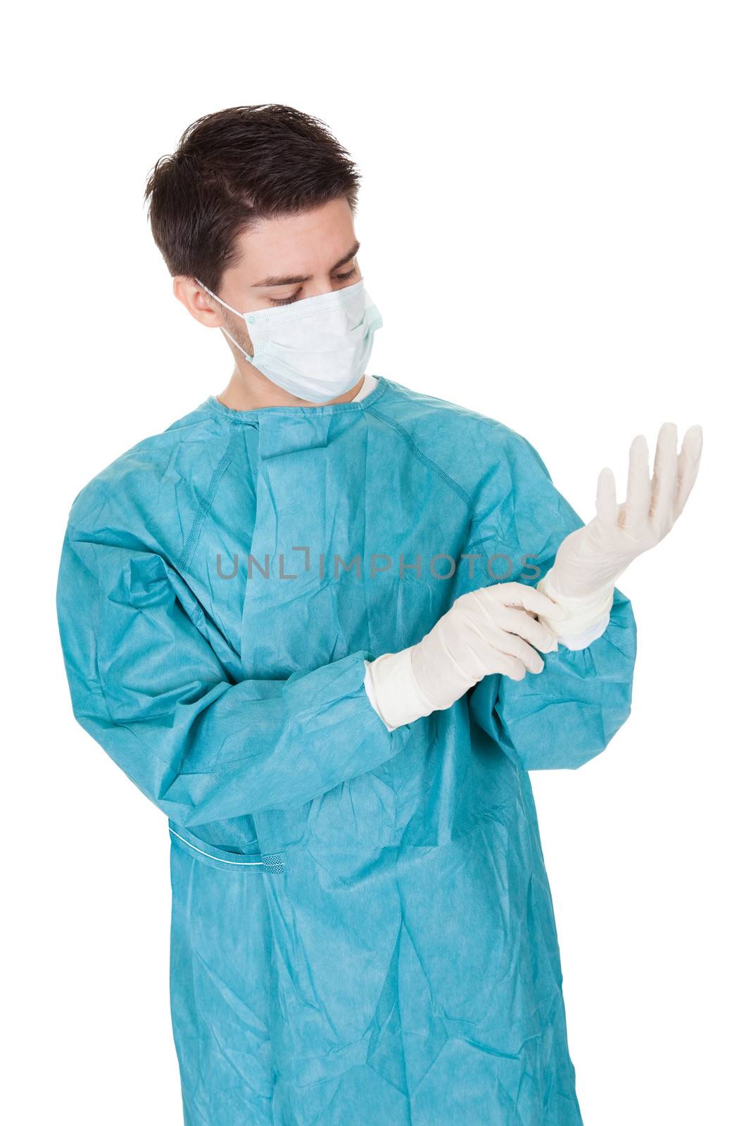 Young male surgeon in a mask and gown putting on disposable surgical gloves before going in to theatre isolated on white