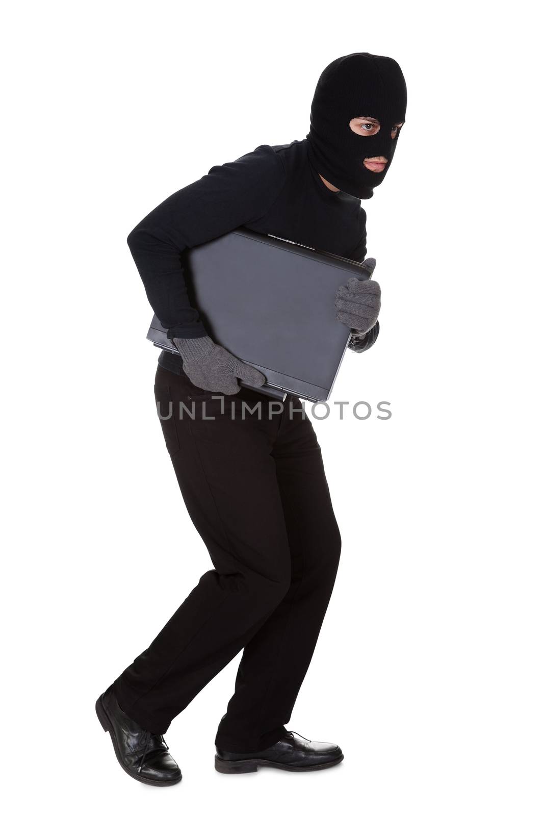 Thief dressed in black and wearing a balaclava stealing a laptop computer and making a furtive escape isolated on white