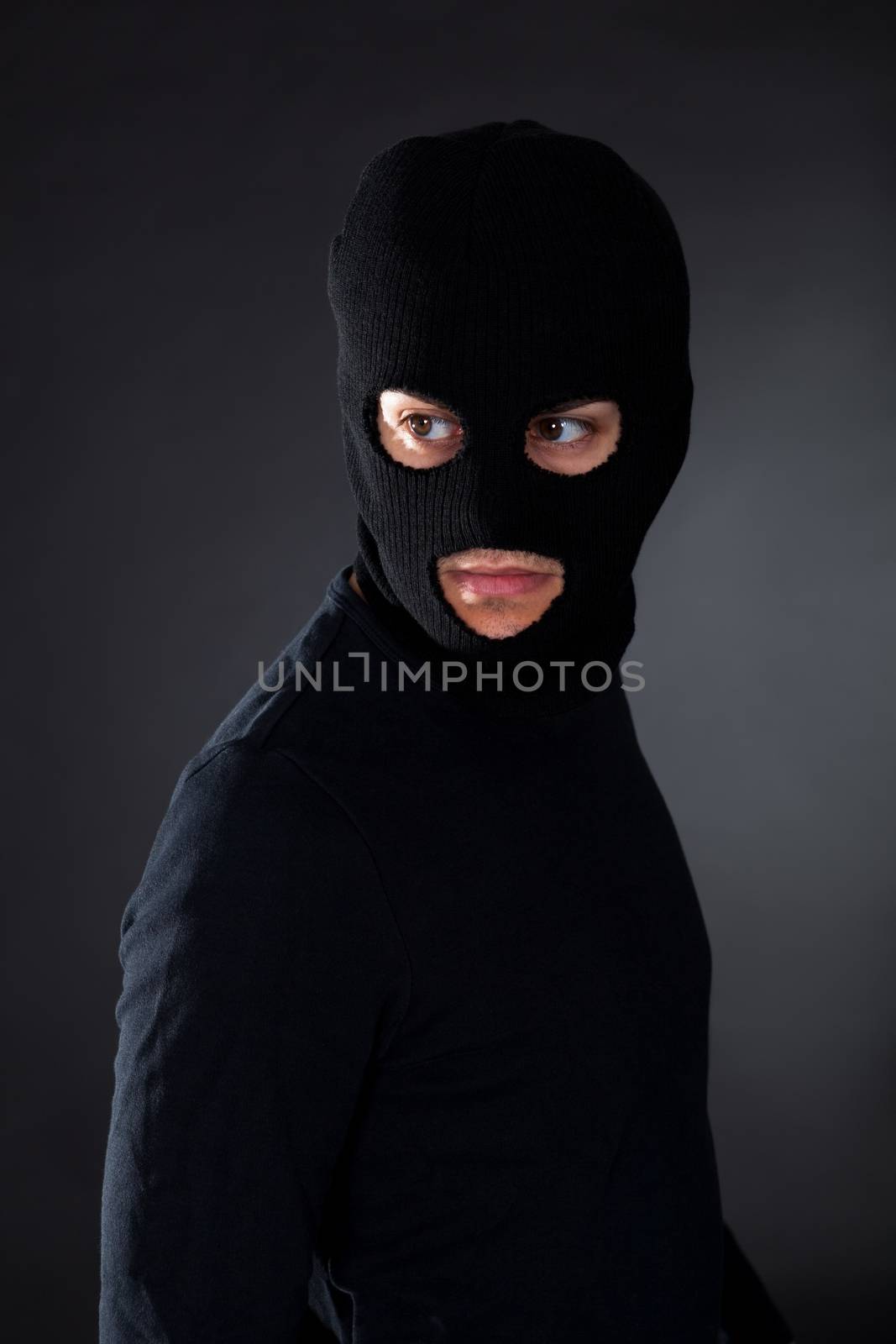 Thief wearing a balaclava dressed in blacked moving stealthily through the darkness as he prepares to commit robbery