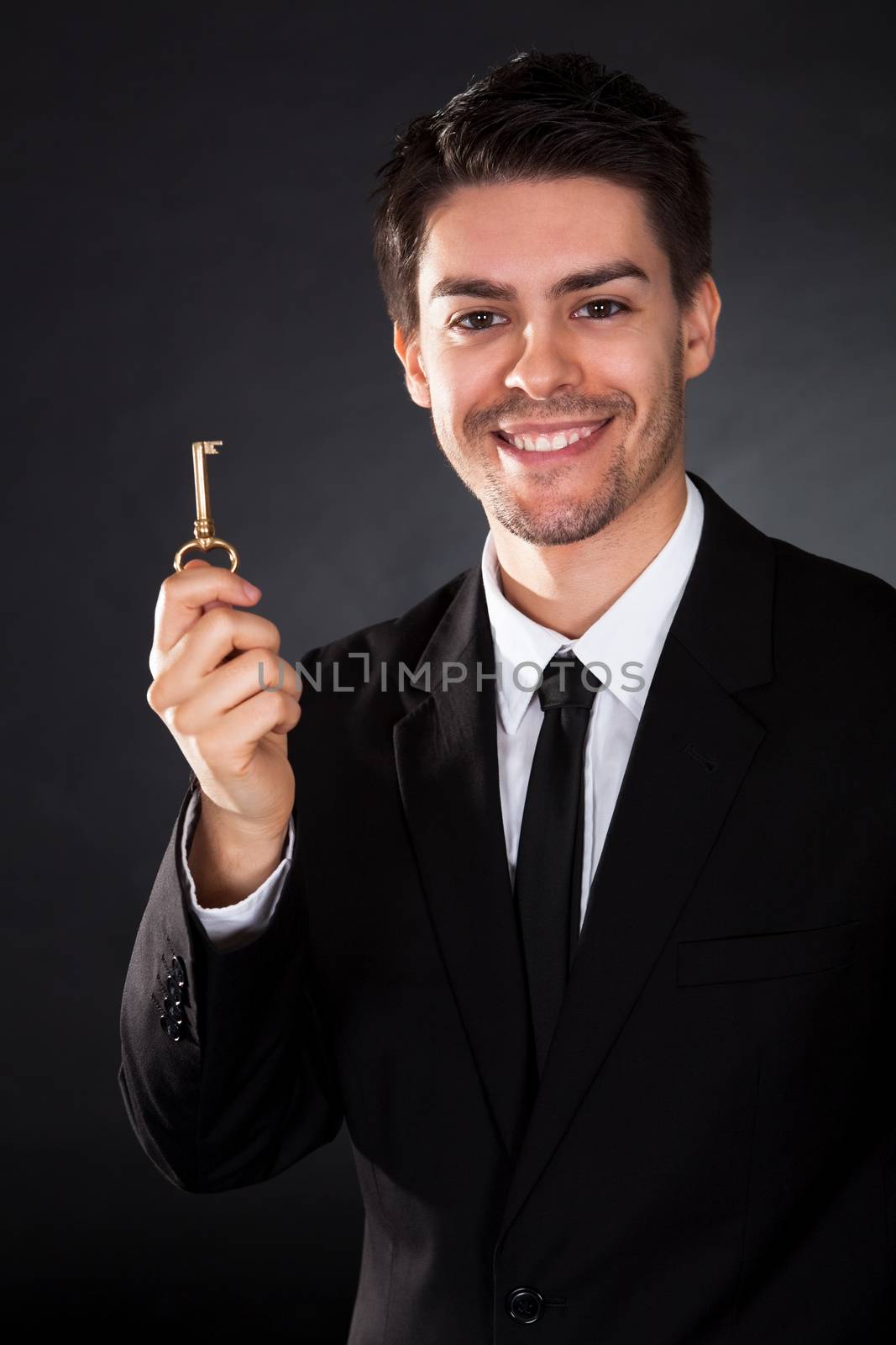 Smiling young businessman holding up a golden key in his hand