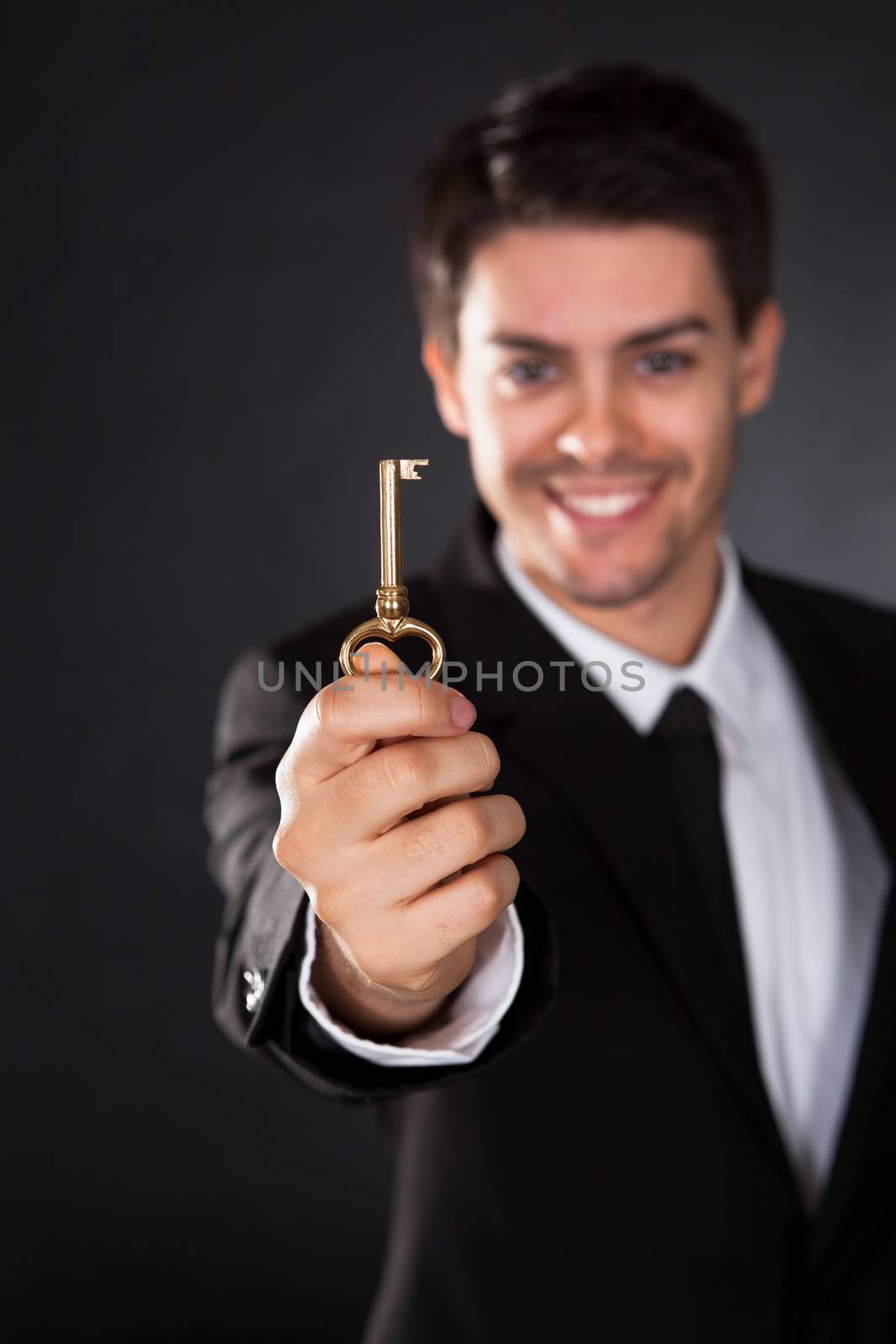 Smiling young businessman holding up a golden key in his hand