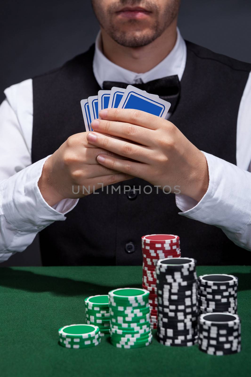 Cropped view of a poker player on a winning streak sitting at a gaming table holding his hand of cards with large stacks of tokens