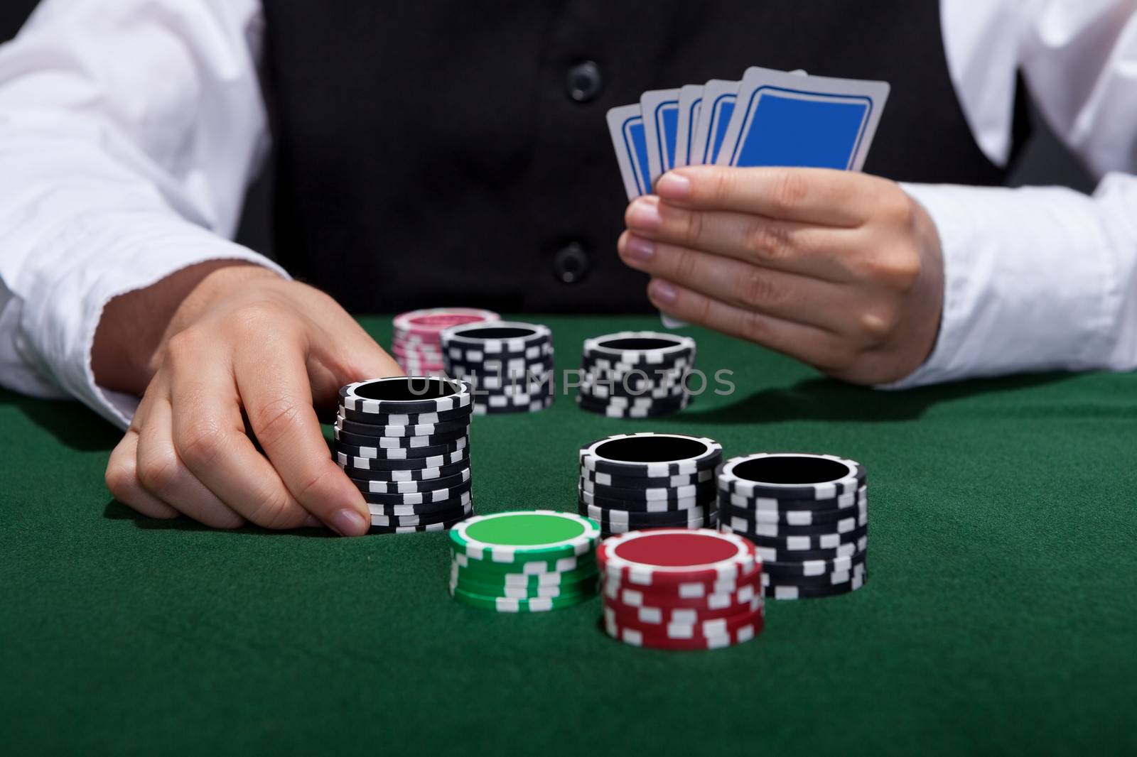 Male poker player about to place a bet moving a stack of tokens towards the centre of the gaming table with his free hand