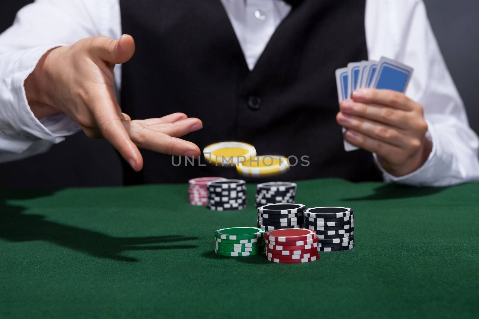 Poker player increasing his stakes throwing tokens onto the gaming table to meet or beat his opponents wager to stay in the game