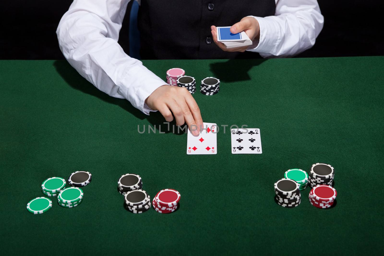 Croupier dealing cards in a poker game placing them face up on the green baize of the gaming table