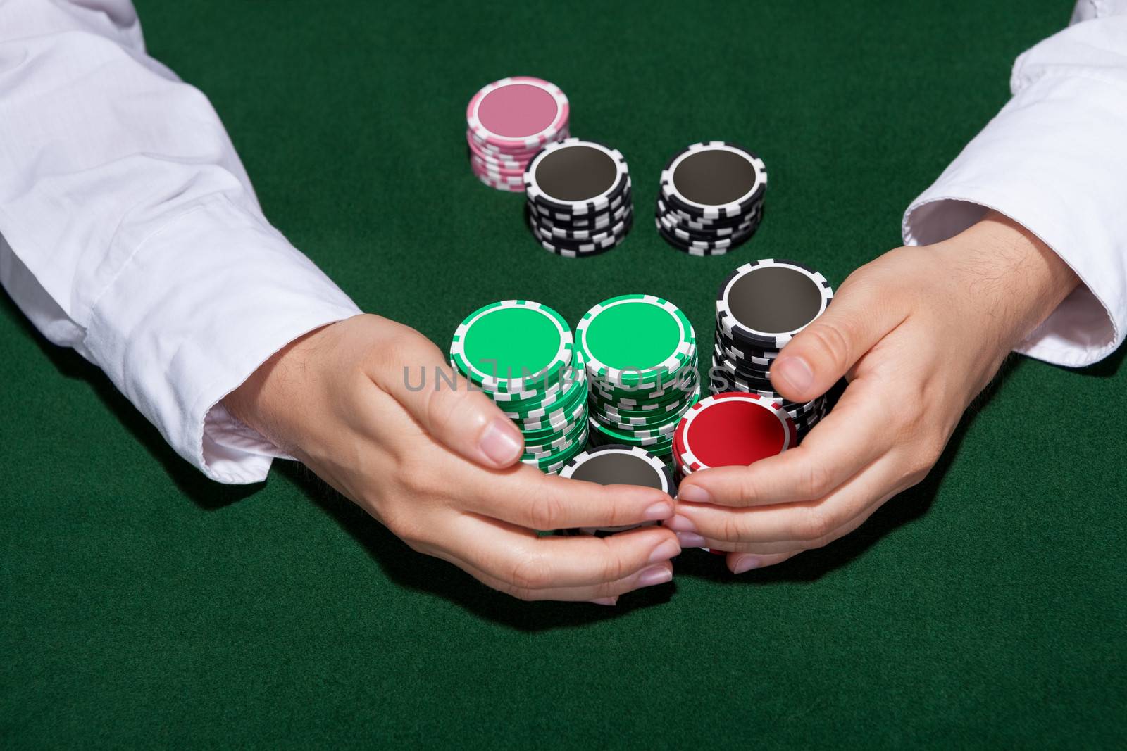 Croupier collecting in the bets at a casino table with his hands encircling various stacks of tokens or chips
