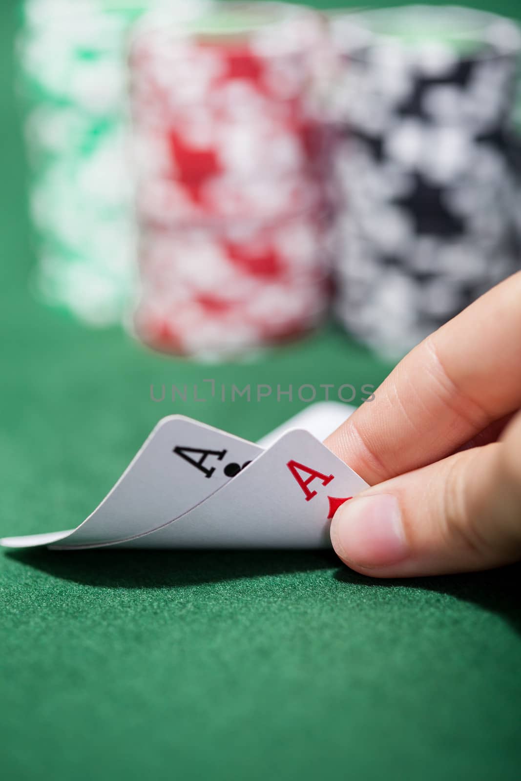 Hand of a male poker player lifting the corners of two cards on the green felt checking a pair of aces