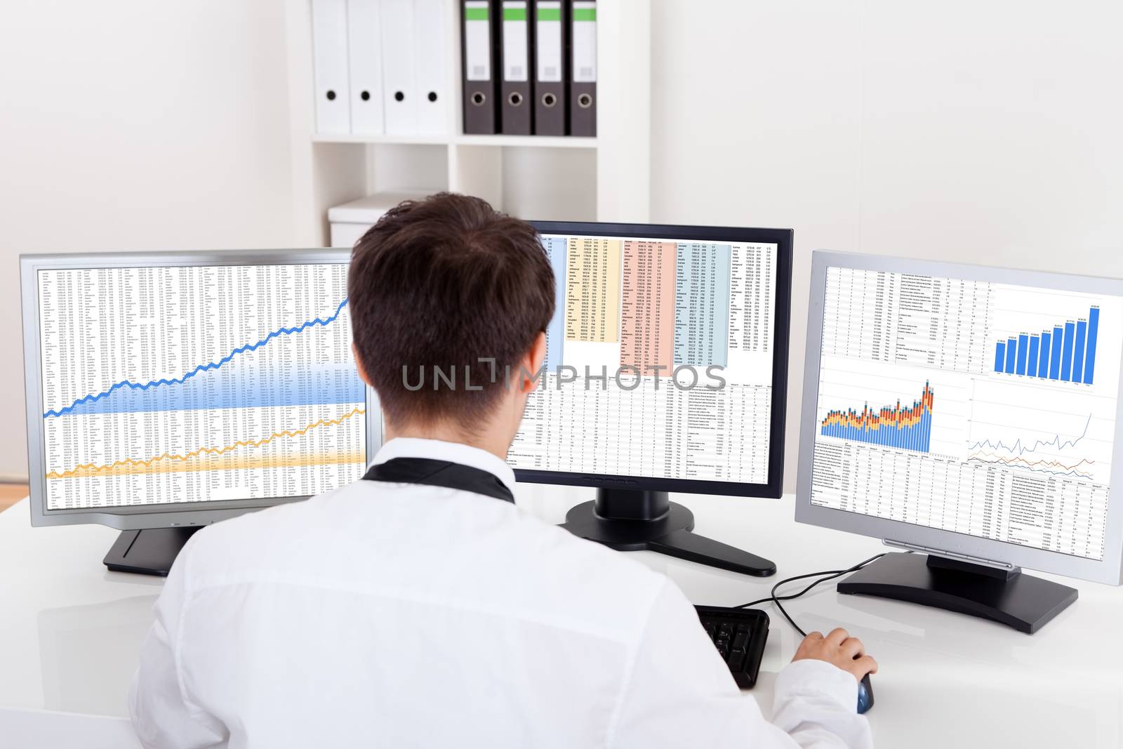 Over the shoulder view of the computer screens of a stock broker trading in a bull market showing ascending graphs