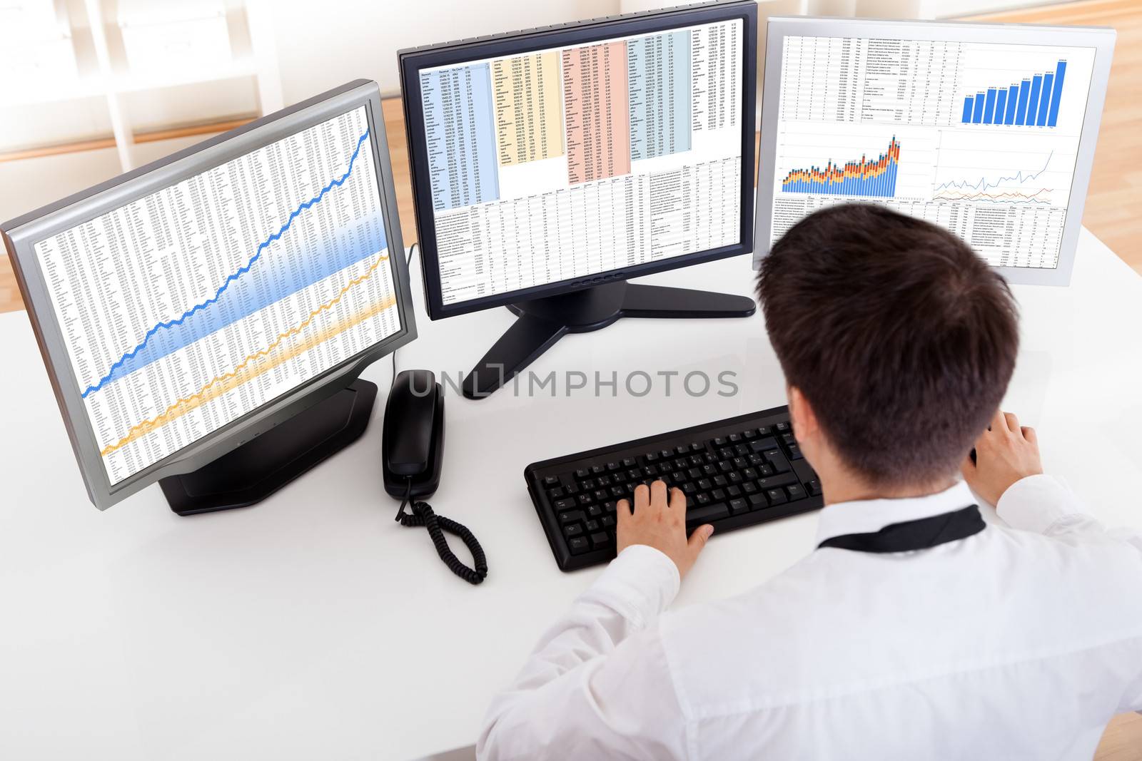 Over the shoulder view of the computer screens of a stock broker trading in a bull market showing ascending graphs